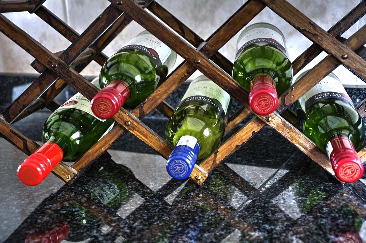 Adega climatizada pequena com garrafas de vinho deitadas em suporte de madeira sobre a bancada