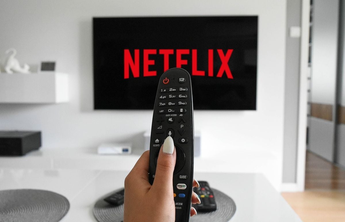 Mão segurando controle remoto em frente a uma TV com o app da Netflix aberto