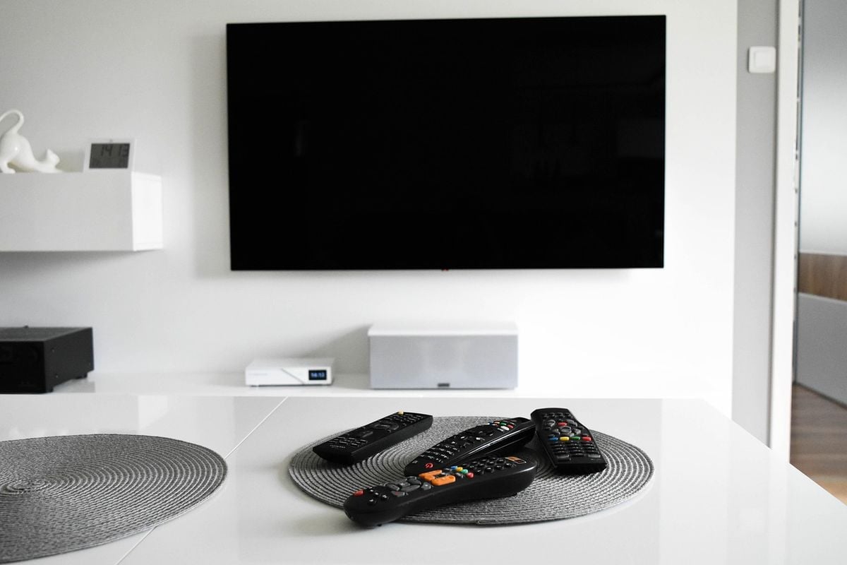 TV smart instalada na parede de uma sala clara, com controles remotos sobre a mesa
