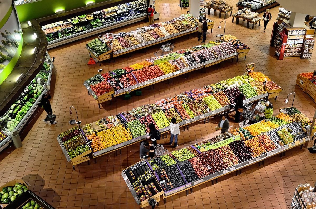Interior de supermercado amplo e climatizado, com corredores de frutas