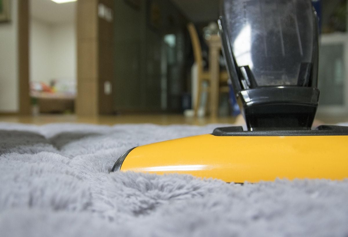 Aspirador portátil amarelo e preto apoiado sobre tapete felpudo cinza